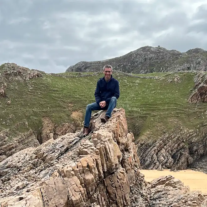 Charlie Cox sitting on a rocky coastal outcrop